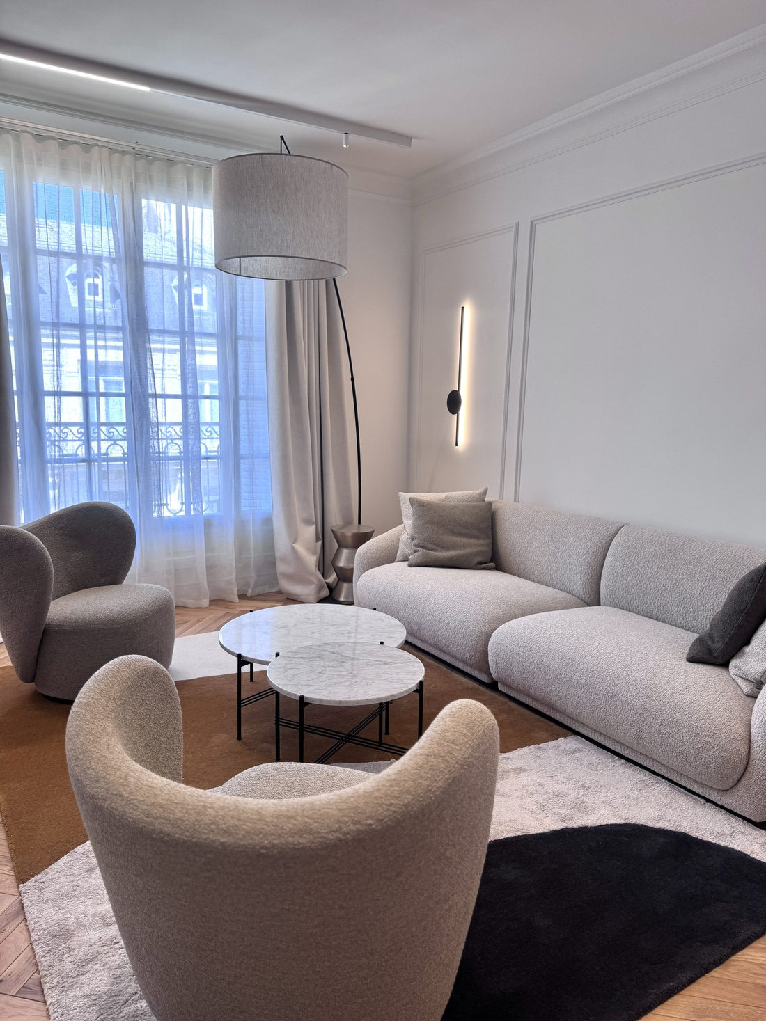 Salon du duplex Périer : canapé clair, fauteuils bouclés et fenêtres