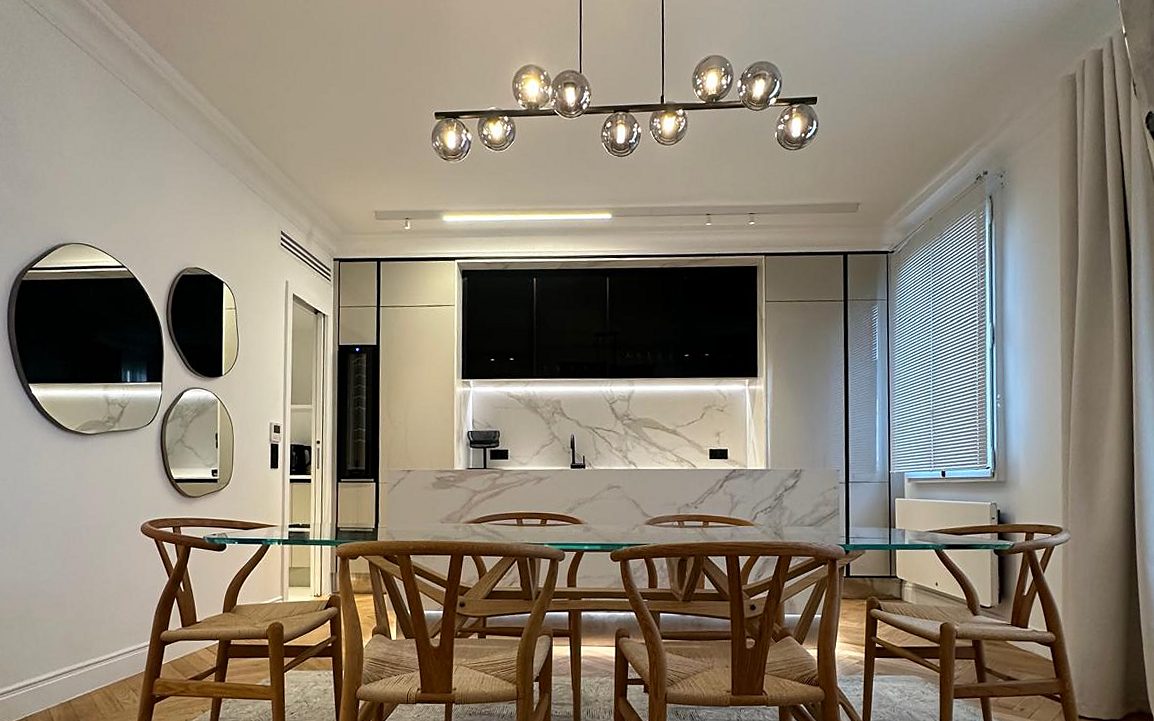 Salle à manger du duplex Périer : table en verre, chaises en bois et cuisine en arrière-plan